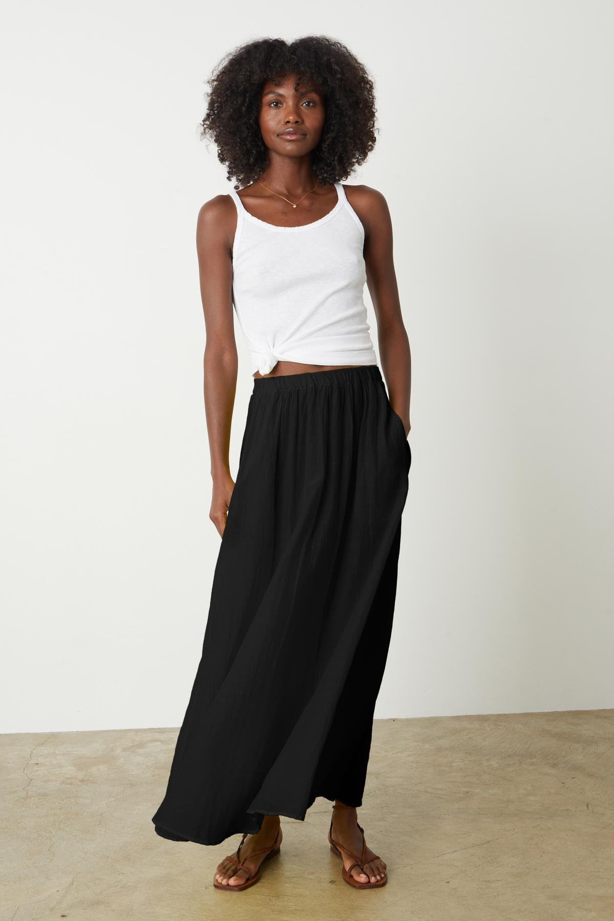   A woman wearing a black Velvet by Graham & Spencer MARIELA MAXI SKIRT and white tank top tied in front 