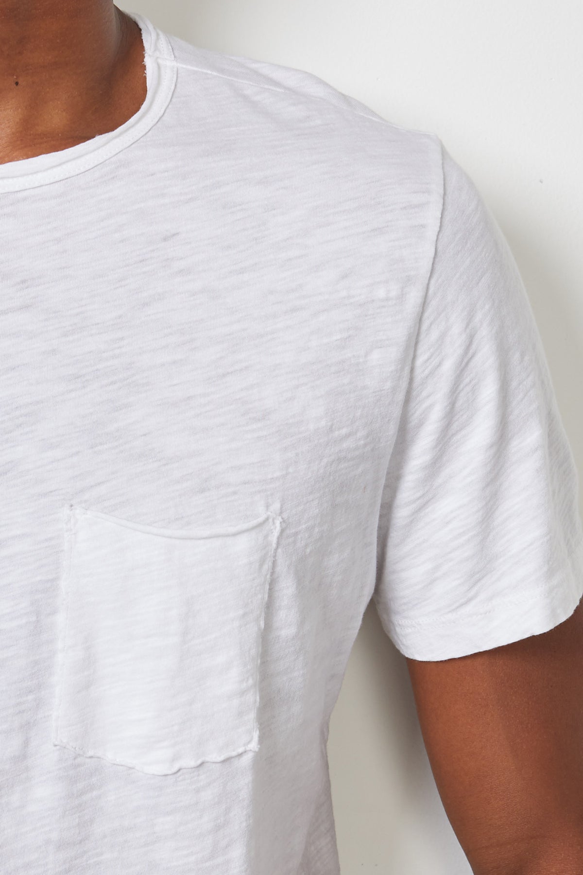   Close-up of a person wearing a white CHAD TEE from Velvet by Graham & Spencer with raw-edge details, focusing on the shoulder and chest area. 