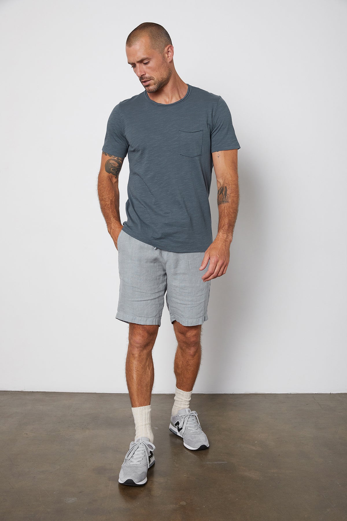   Chad slub cotton tee with raw edges and front pocket in malachite, with Jonathan shorts in chambray with model's hand in pocket. 
