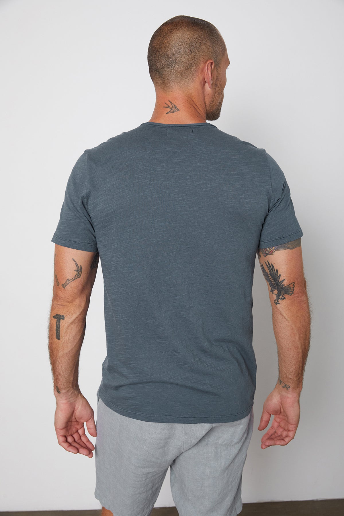 Back of Chad slub cotton tee with raw edges and front pocket in malachite, with Jonathan shorts in chambray.-25328431759553
