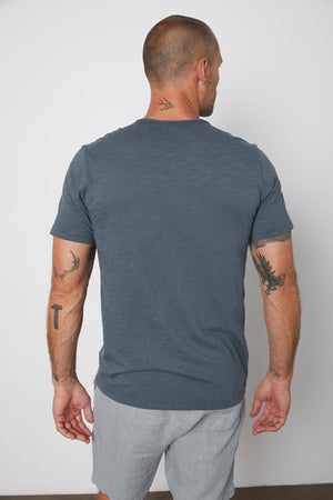 Back of Chad slub cotton tee with raw edges and front pocket in malachite, with Jonathan shorts in chambray.