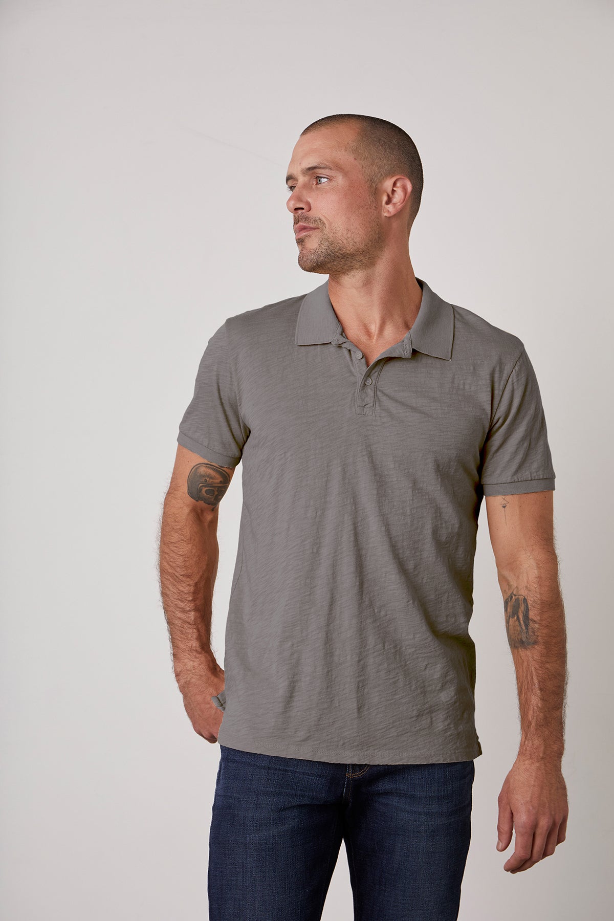   A man wearing a classic NIKO POLO shirt silhouette in a gray color, paired with jeans. 