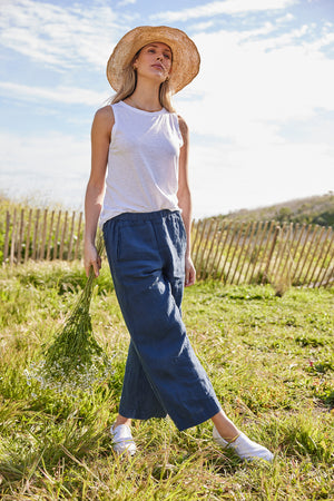 A woman wearing a Velvet by Graham & Spencer straw hat and blue linen pants in a field, showcasing her spring/summer style and western charm.