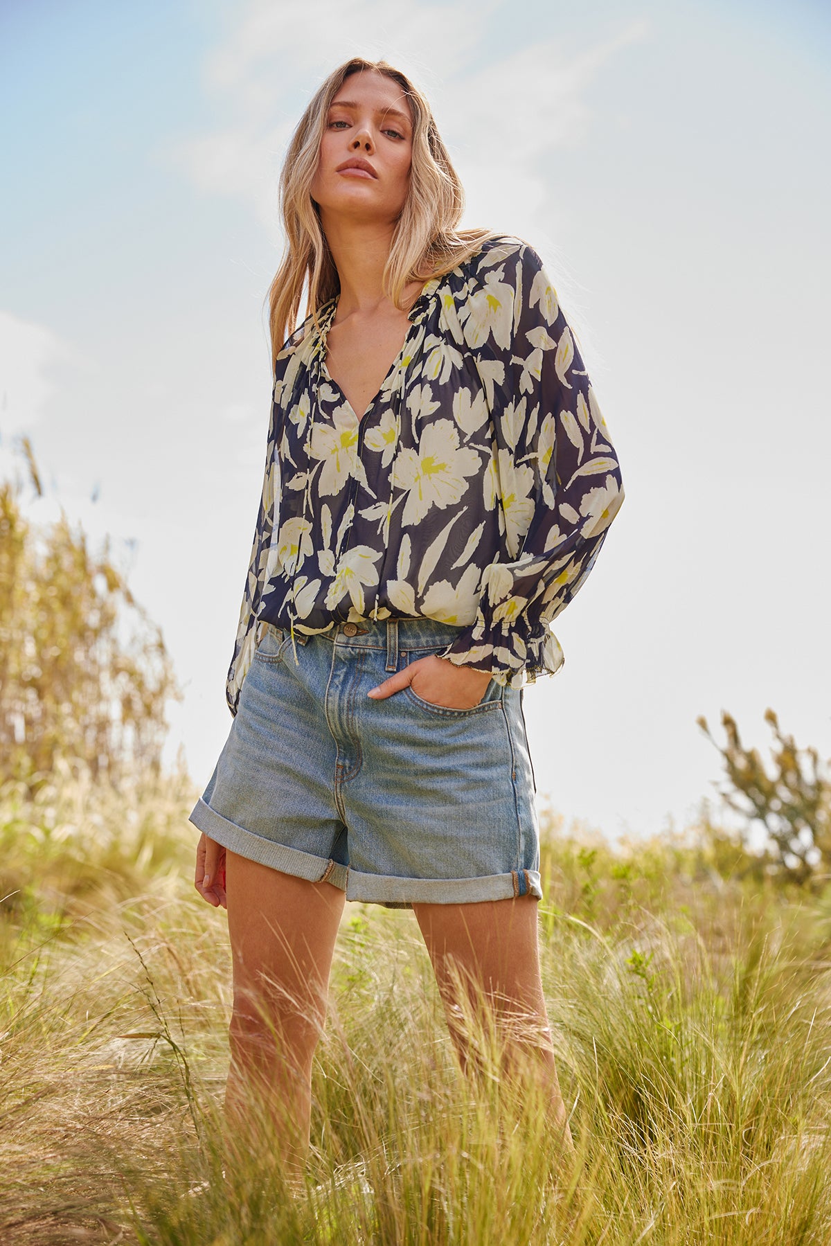 a woman in denim shorts standing in a field wearing the MILEY PRINTED TOP by Velvet by Graham & Spencer.-26182385139905