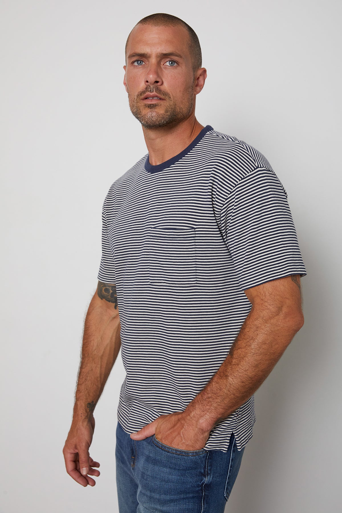 Eli striped crew neck tee with front patch pocket and  navy contrast rib band around neckline model standing with hand in jeans pocket.-25003075240129