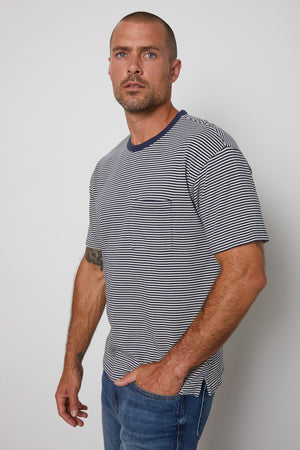 Eli striped crew neck tee with front patch pocket and  navy contrast rib band around neckline model standing with hand in jeans pocket.
