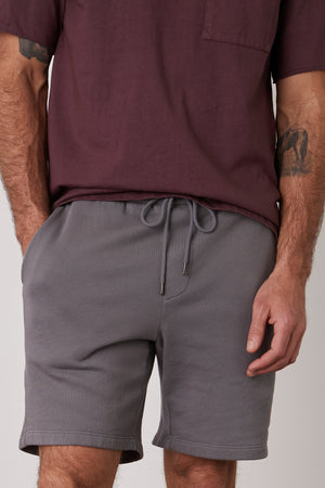 A man wearing grey JAXSON DRAWSTRING SHORTs and a maroon t-shirt in a casual short, with extra soft fleece interior by Velvet by Graham & Spencer.
