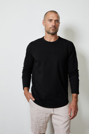 A man with a shaved head and beard is wearing a black long-sleeve shirt and Velvet by Graham & Spencer MAXWELL LINEN SHORT with an elastic waistline, standing against a plain white background.