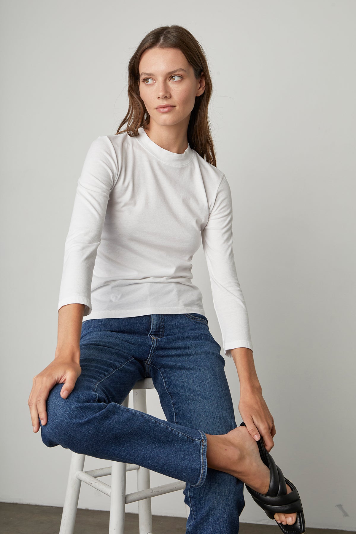 A woman in Los Angeles is sitting on a stool wearing Velvet by Graham & Spencer's VICTORIA HI RISE STRAIGHT LEG JEAN and a white t-shirt.-23514539000001
