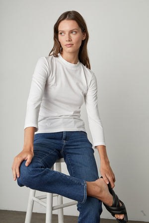 A woman in Los Angeles is sitting on a stool wearing Velvet by Graham & Spencer's VICTORIA HI RISE STRAIGHT LEG JEAN and a white t-shirt.