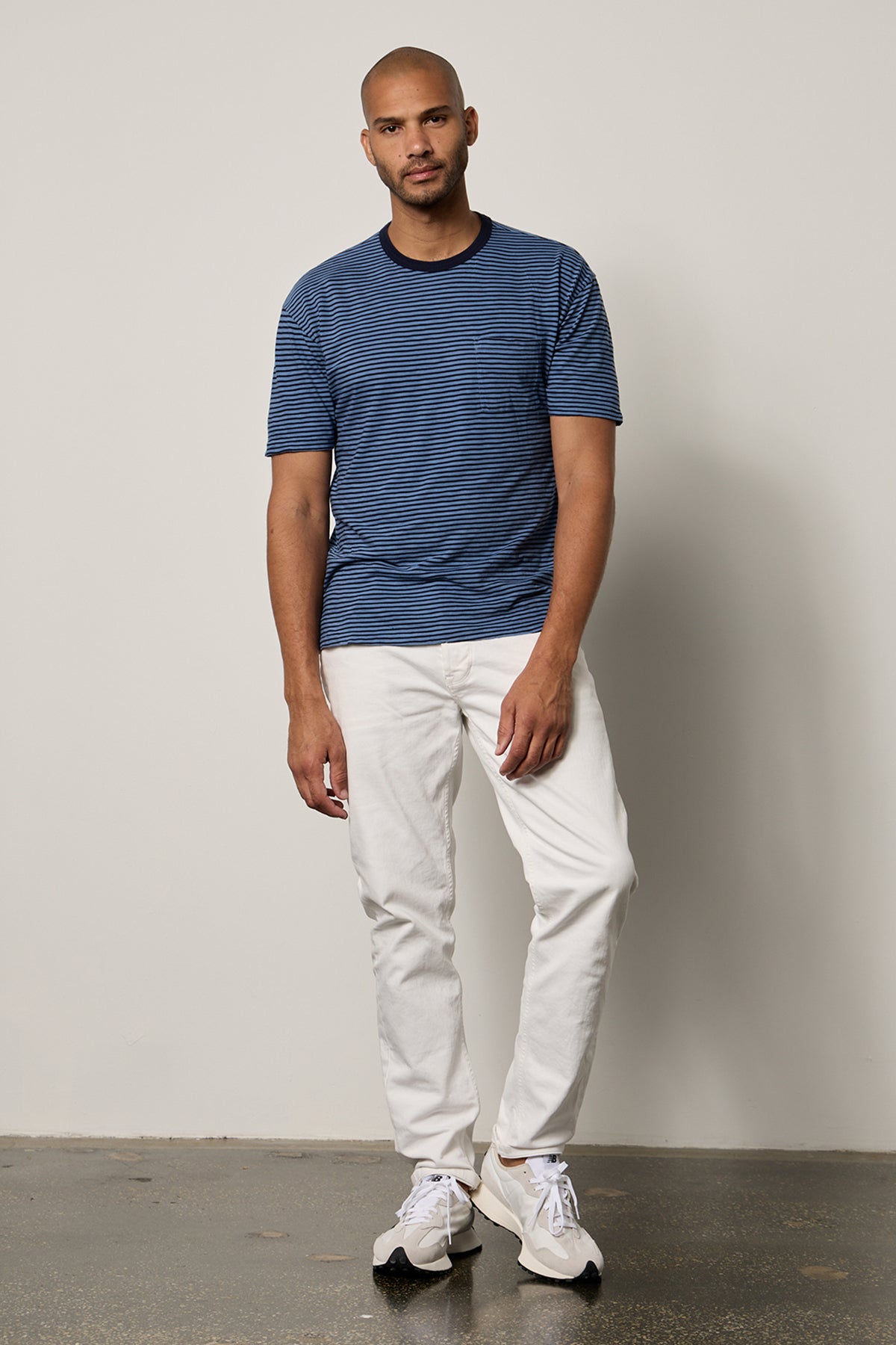   Jeremy Crew Neck Tee with medium and dark blue stripes, front pocket, paired with white denim full length front with New Balance sneakers 