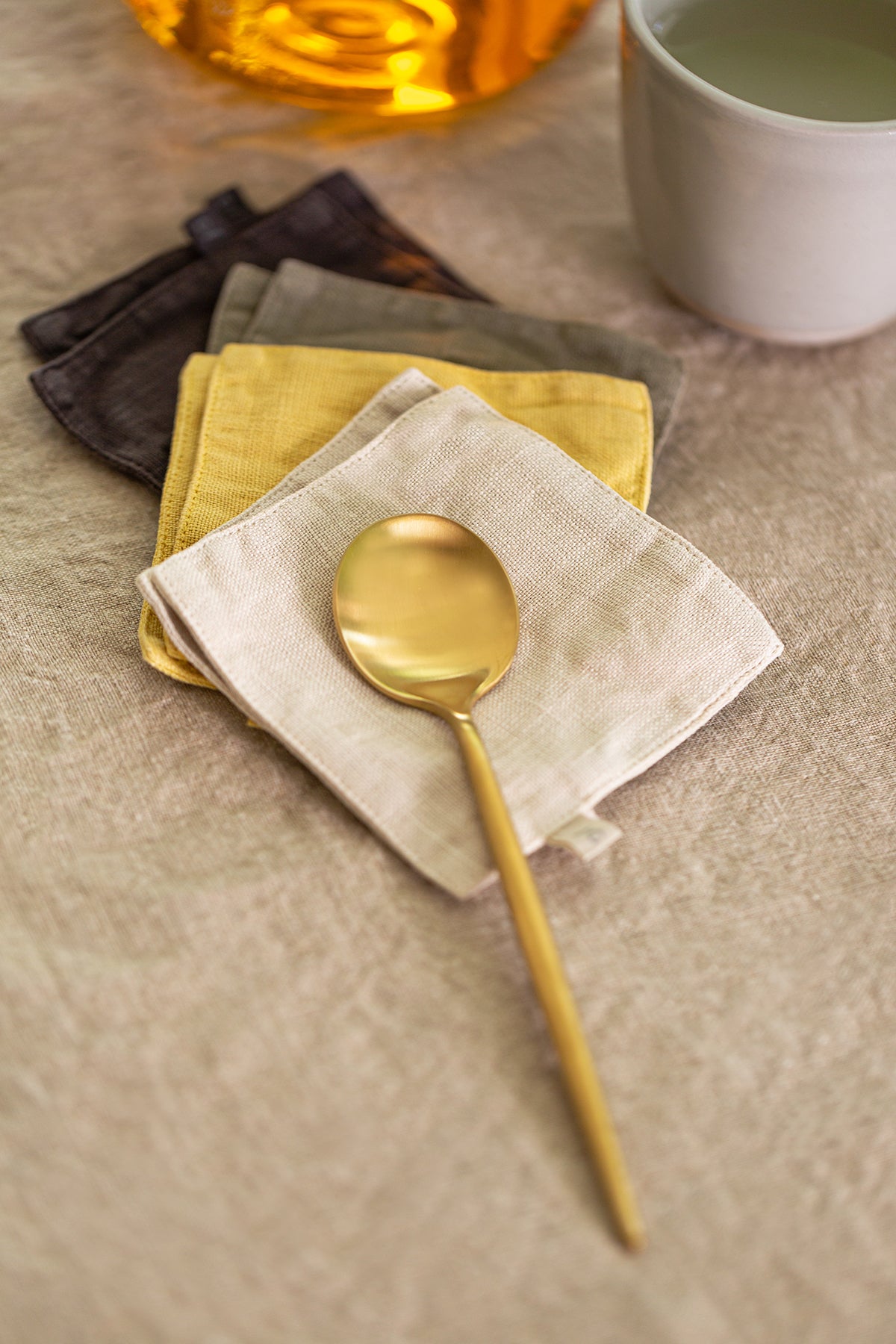 a set of 4 LINEN COASTERS by Jenny Graham Home on a napkin next to a cup of tea.-14899252297921