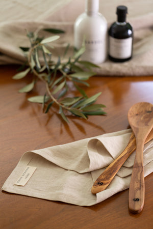A Jenny Graham Home linen napkin, an everyday kitchen essential, sits on a wooden table with a luxe finish.