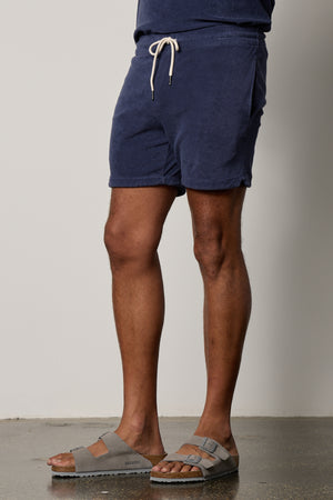 A man wearing a pair of OZZIE TERRY SHORT shorts and sandals.