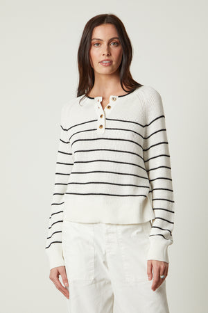 a woman wearing a Velvet by Graham & Spencer KIERRA HENLEY SWEATER, white and black striped sweater, and white pants.