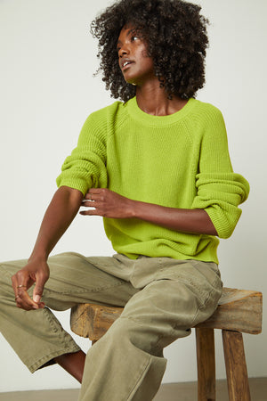 A woman is sitting on a stool in a Velvet by Graham & Spencer LINAH CREW NECK SWEATER in lime green.