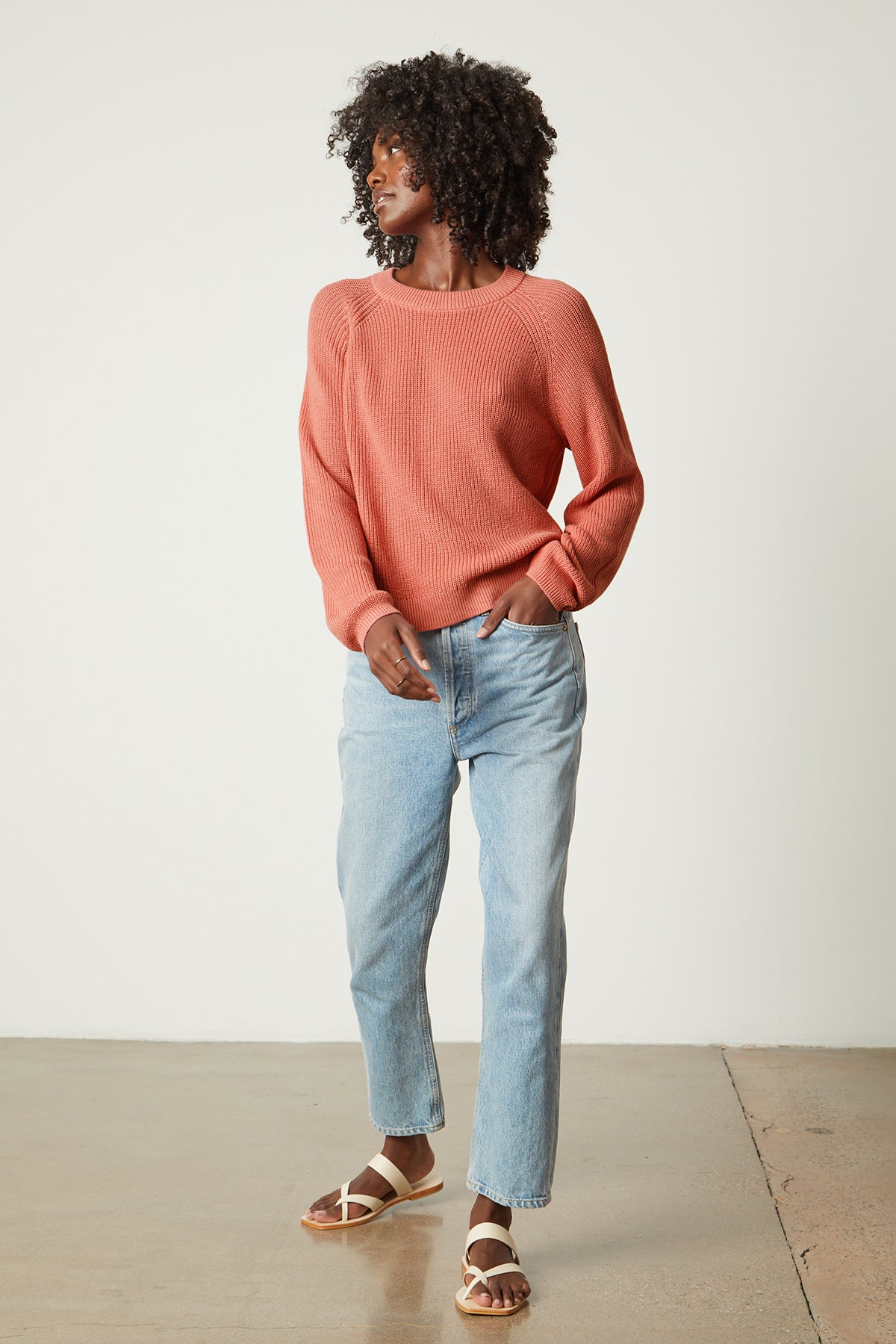 a woman in a LINAH CREW NECK SWEATER by Velvet by Graham & Spencer and jeans is standing in front of a white wall.-25916268839105