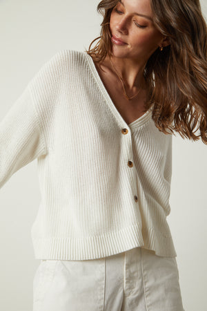 The model is wearing a YASMINE BUTTON FRONT CARDIGAN and white pants.
