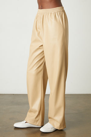 A woman wearing Jenna Vegan Leather Wide Leg Pants by Velvet by Graham & Spencer and white sneakers in holiday style.