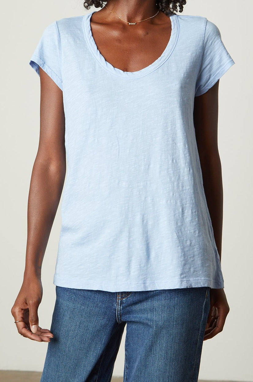 A person is wearing a light blue, short-sleeved, cotton slub fabric KIRA TEE by Velvet by Graham & Spencer with a scoop neckline and blue jeans. The person's skin tone is medium brown. This ensemble is a perfect example of everyday wear.