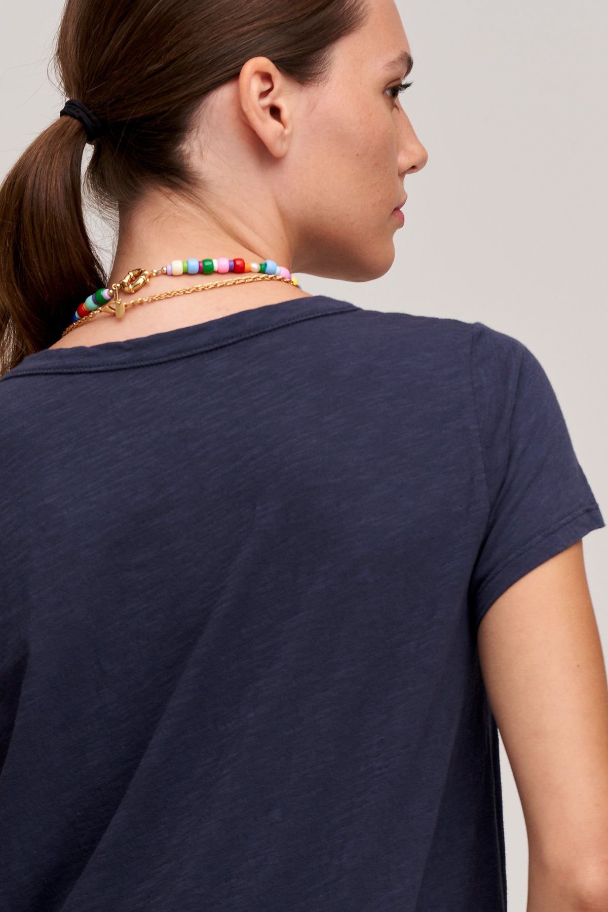 The back view of a woman wearing a TILLY ORIGINAL SLUB CREW NECK TEE by Velvet by Graham & Spencer with colorful beads.-24532951695553