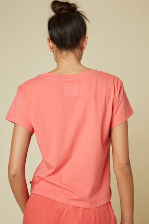 A person with dark hair in a bun is shown from the back, wearing a Velvet by Jenny Graham VENICE TEE and matching bottoms made of organic cotton against a plain beige background.