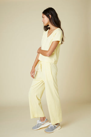 A woman stands in profile wearing a light yellow VENICE TEE by Velvet by Jenny Graham made from organic cotton and gray sneakers.