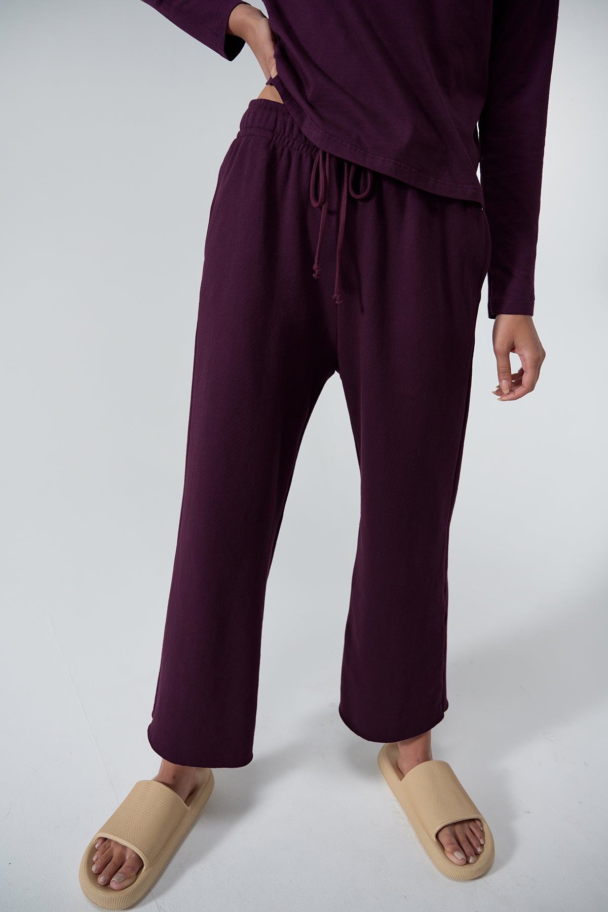 Person wearing a long-sleeve purple outfit and beige slip-on sandals, featuring MONTECITO SWEATPANT by Velvet by Jenny Graham made of organic cotton. Only the lower half of their body is visible.-24063809061057