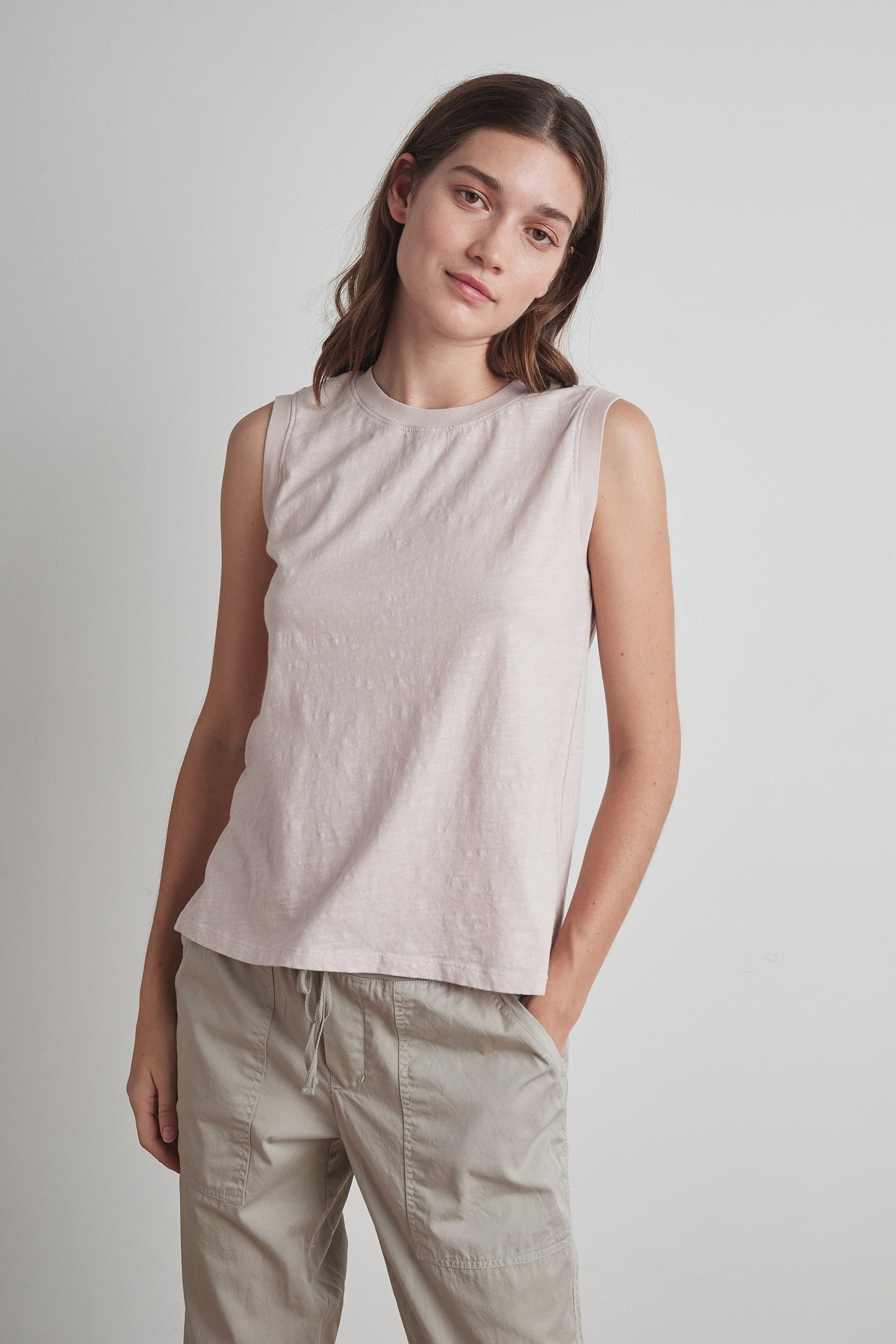 A woman with long hair wearing a light pink ELLEN VINTAGE SLUB TANK TOP by Velvet by Graham & Spencer and light gray pants stands against a plain background.-23985126801601