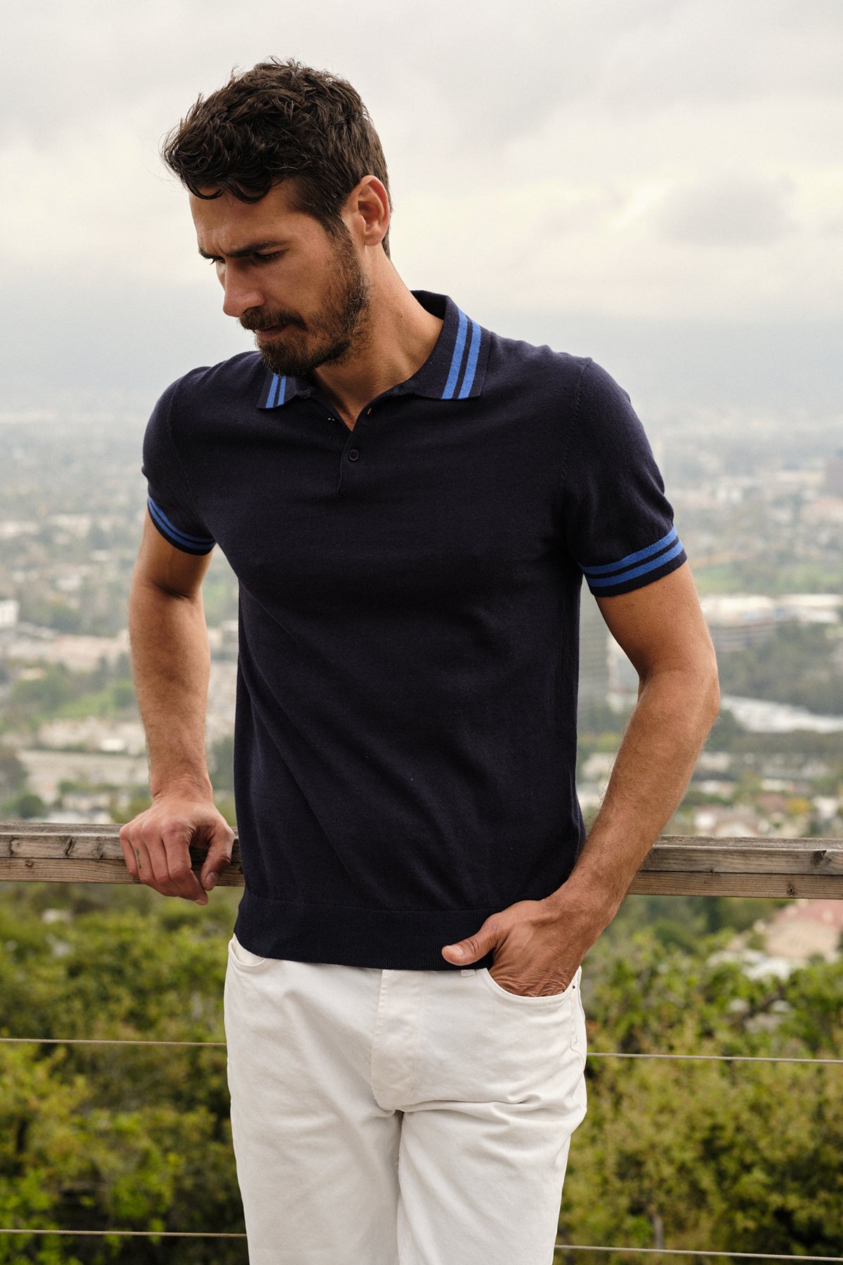 Lifestyle image of model standing outdoors wearing Hogan Polo in navy linen blend with double stripes on collar and sleeves with white denim front-26249274917057