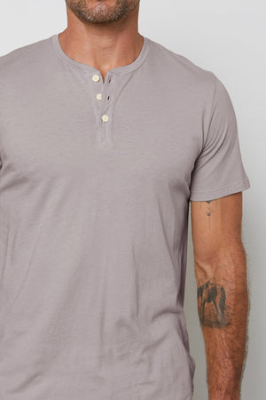 A man wearing a classic grey Velvet by Graham & Spencer Fulton Short Sleeve Henley made of cotton jersey.