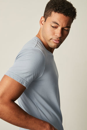 A person wearing a SAMSEN WHISPER CLASSIC V-NECK TEE by Velvet by Graham & Spencer looks downward with a neutral expression against a plain background.