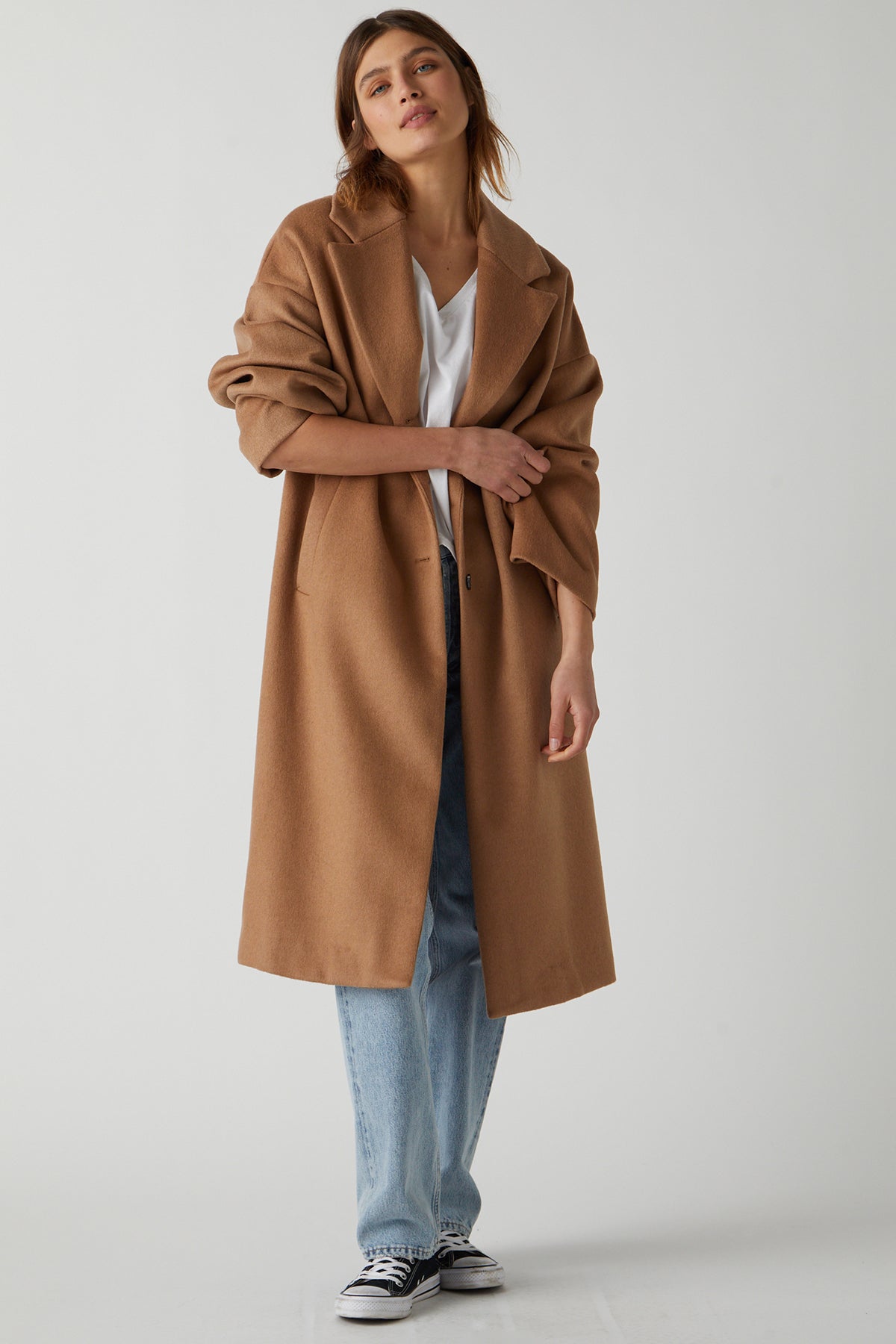 A person wearing a chic HUNTINGTON COAT by Velvet by Jenny Graham, made of soft wool blend, a white t-shirt, light blue jeans, and black and white sneakers stands against a plain backdrop.-25483423416513