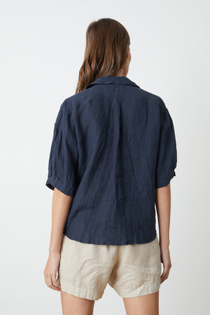 the back view of a woman wearing a Velvet by Graham & Spencer MARIA LINEN BUTTON-UP SHIRT and tan shorts.