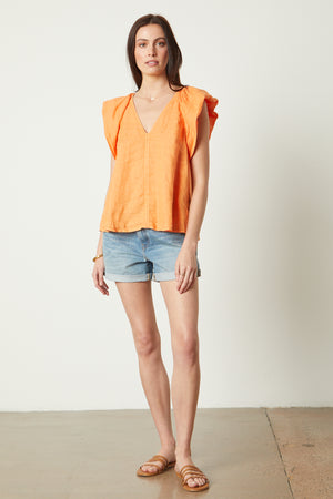 a woman wearing an AVA LINEN V-NECK TOP by Velvet by Graham & Spencer and denim shorts.