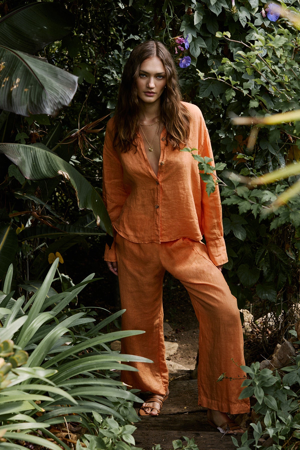   Women standing outdoors surrounded by trees wearing Eden shirt in orange heat with Lola pant, necklaces and sandals full length front 