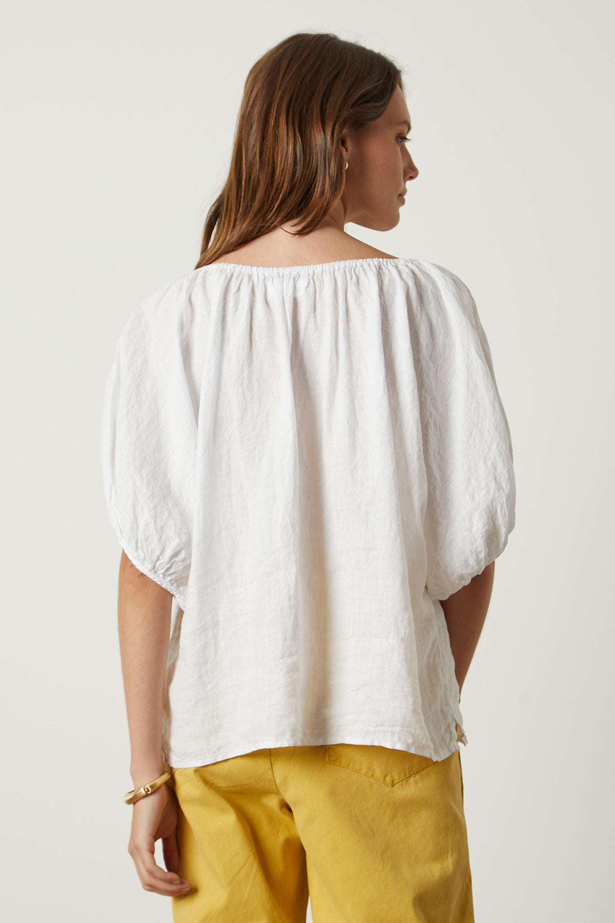 The back view of a woman wearing a Velvet by Graham & Spencer JANINE LINEN TOP and yellow pants.-26142774853825
