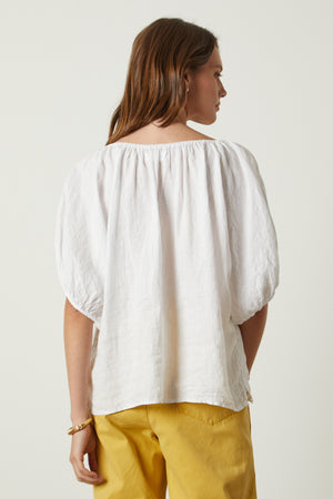 The back view of a woman wearing a Velvet by Graham & Spencer JANINE LINEN TOP and yellow pants.