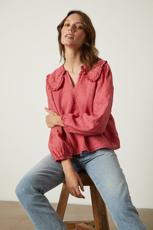 Model sitting on stool wearing Sofia linen top in punch with light blue denim front