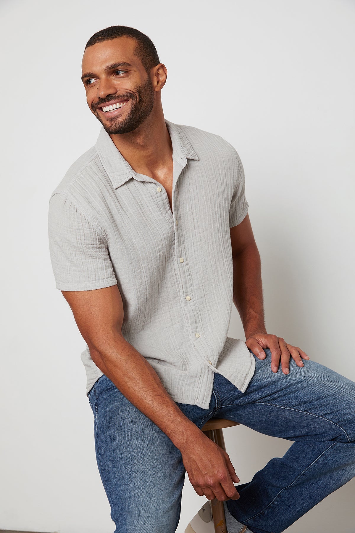   Cotton gauze Christian button up shirt in light grey with model smiling and sitting on stool. 