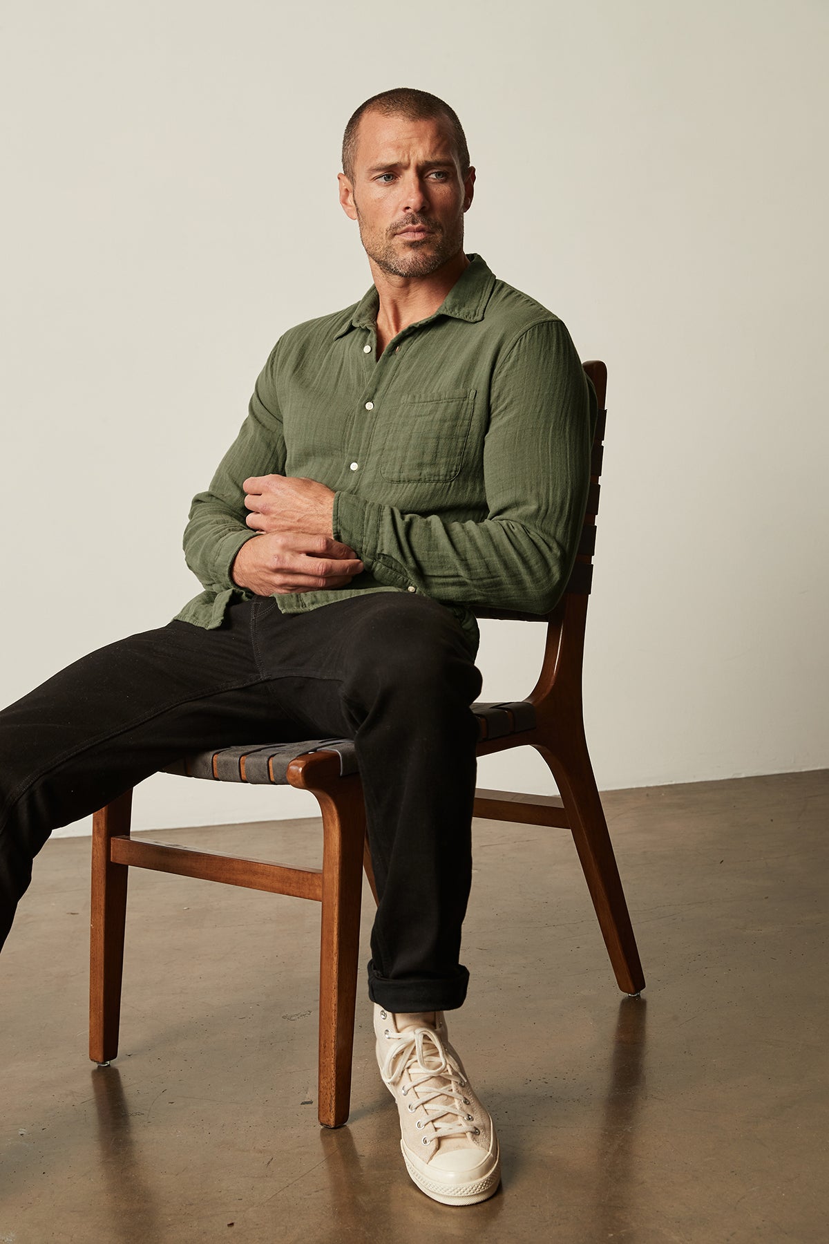   A man sitting on a chair in a green Velvet by Graham & Spencer ELTON BUTTON-UP SHIRT. 