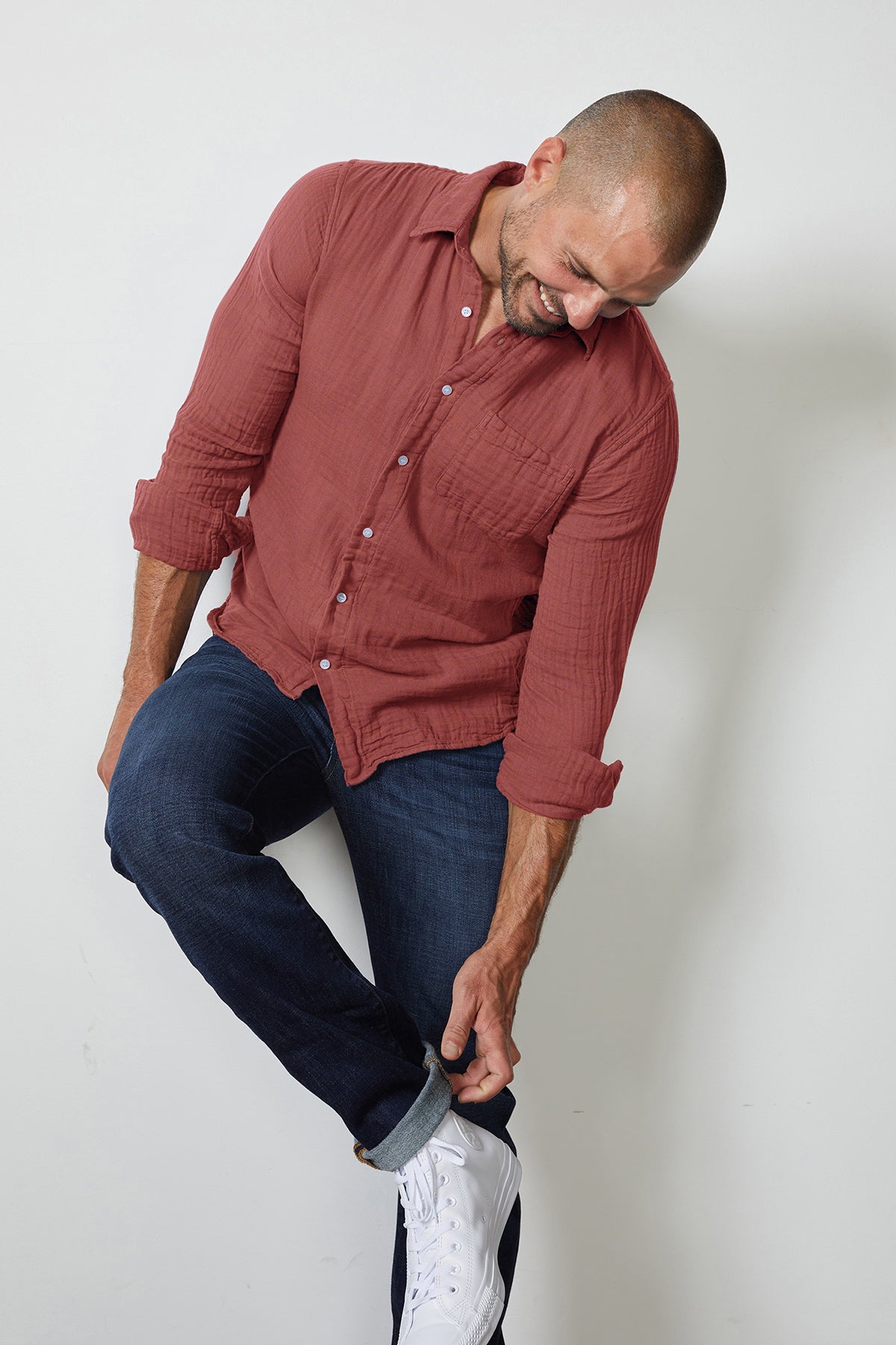 A man in a Velvet by Graham & Spencer ELTON BUTTON-UP SHIRT, made of cotton gauze woven fabric, leaning against a wall.-25793275723969