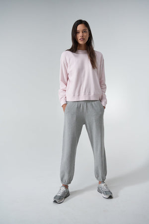 A woman stands in a neutral pose, showcasing a YNEZ SWEATSHIRT by Velvet by Jenny Graham made from cozy fleece, paired with gray jogger pants and matching sneakers, against a plain white background.